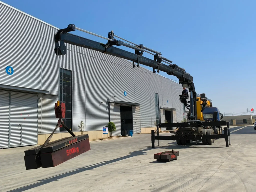 A Zorylift SQZ300A.5 15-ton knuckle boom crane, a type of lorry mounted crane, lifts a 500kg test weight outside a factory building. This black 15 ton truck mounted crane, specifically a truck mounted knuckle boom crane, showcases its operation.
